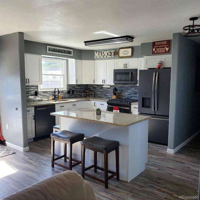 kitchen with white cabinets, black appliances, a kitchen island, dark hardwood / wood-style flooring, and a breakfast bar