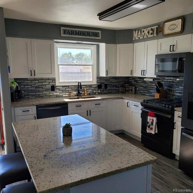 kitchen featuring white cabinets, a center island, black appliances, and light stone countertops