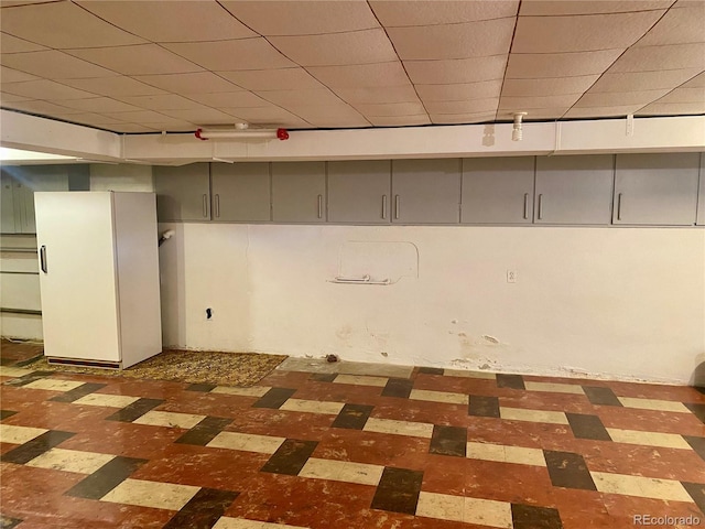 basement featuring a drop ceiling, track lighting, and white fridge