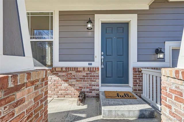 entrance to property with a porch and brick siding
