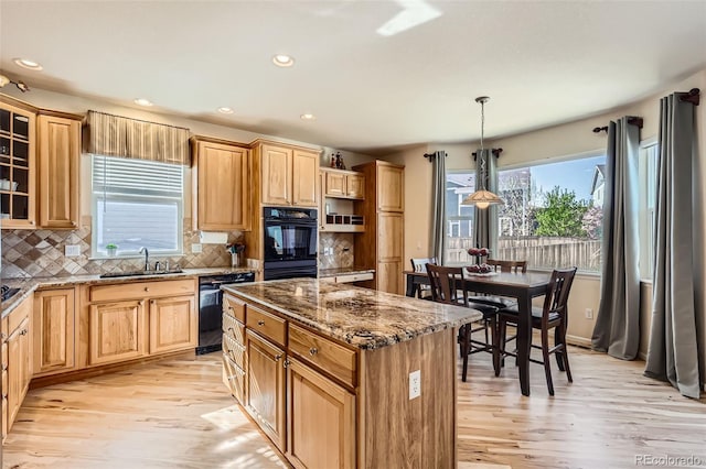 kitchen featuring dark stone counters, a sink, black appliances, light wood-style floors, and a kitchen island