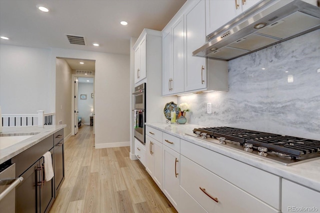 527 Felicity Loop, Castle Rock, CO 80109 - kitchen with under cabinet range hood, stainless steel appliances, decorative backsplash, light wood finished floors, and white cabinets