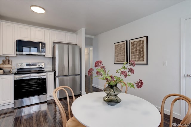 kitchen with dark countertops, appliances with stainless steel finishes, white cabinets, baseboards, and dark wood-style flooring