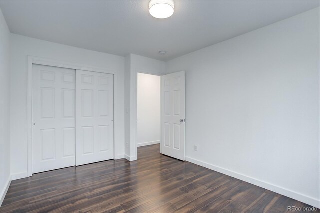 unfurnished bedroom featuring baseboards, dark wood-style flooring, and a closet