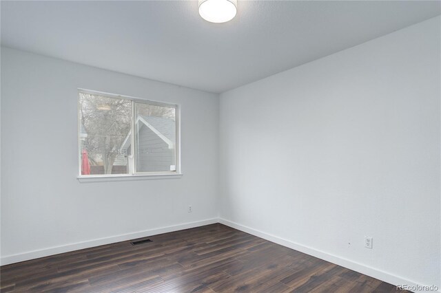 empty room with visible vents, baseboards, and dark wood finished floors