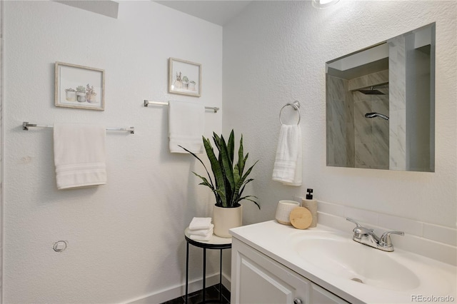 full bathroom with a tile shower, vanity, and baseboards