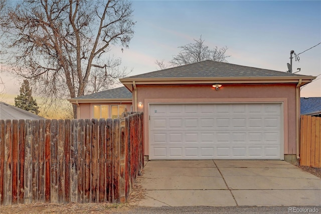 garage at dusk featuring concrete driveway and fence