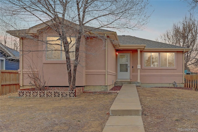 view of front of home featuring stucco siding, a shingled roof, and fence