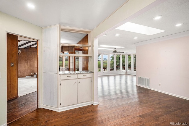 interior space featuring visible vents, wood finished floors, baseboards, ceiling fan, and a skylight