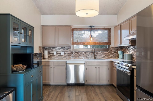 kitchen with sink, tasteful backsplash, wood-type flooring, appliances with stainless steel finishes, and pendant lighting