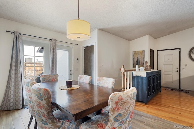 dining room with lofted ceiling, light hardwood / wood-style floors, and a textured ceiling