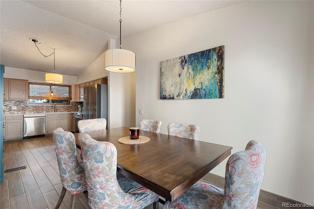 dining area with sink, vaulted ceiling, hardwood / wood-style floors, and a textured ceiling