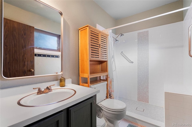 bathroom with a tile shower, vanity, and toilet