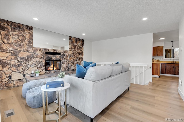 living room with sink, a fireplace, a textured ceiling, and light wood-type flooring