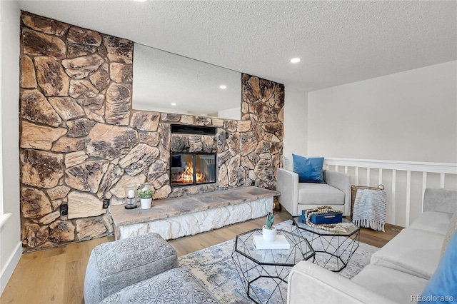 living room featuring a stone fireplace, hardwood / wood-style floors, and a textured ceiling