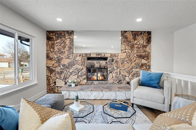 living room with a stone fireplace, hardwood / wood-style floors, and a textured ceiling