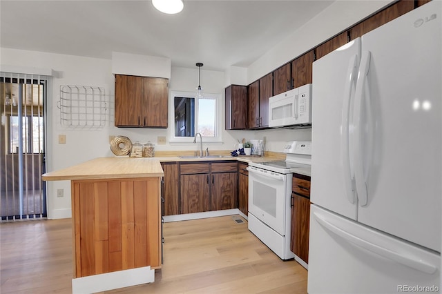 kitchen featuring sink, white appliances, light hardwood / wood-style flooring, and decorative light fixtures