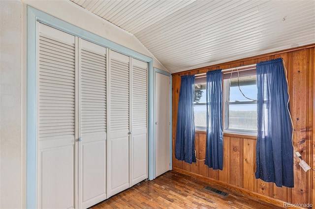 unfurnished bedroom featuring wooden walls, dark hardwood / wood-style floors, and lofted ceiling