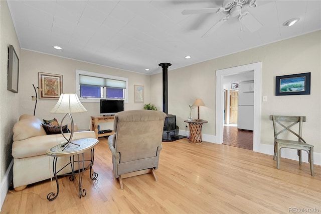 living area with ceiling fan, baseboards, recessed lighting, a wood stove, and light wood-style floors