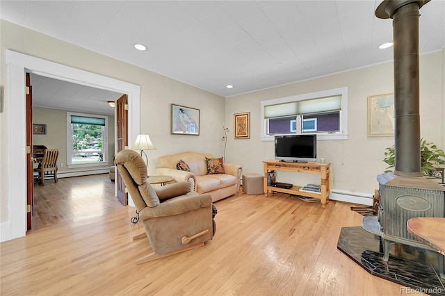 living area with recessed lighting, a baseboard heating unit, a wood stove, and light wood finished floors