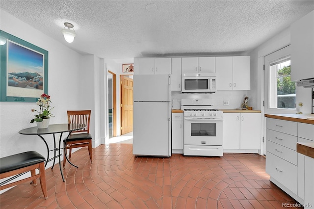 kitchen with white appliances, white cabinetry, light countertops, and brick floor