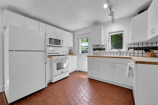 kitchen featuring white appliances, a sink, wood counters, white cabinetry, and backsplash