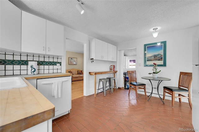 kitchen with decorative backsplash, brick floor, white dishwasher, white cabinets, and a sink