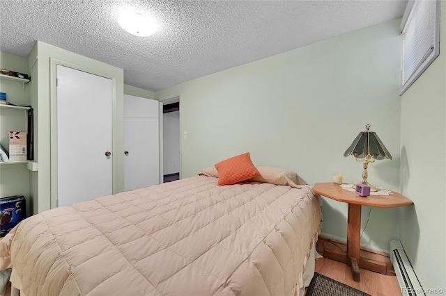 bedroom with a textured ceiling, wood finished floors, and a baseboard radiator