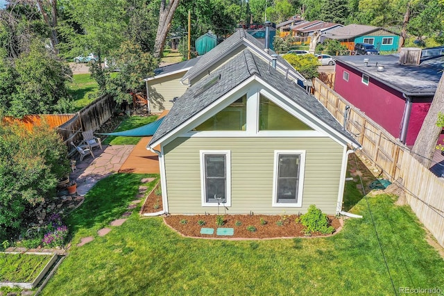 rear view of house featuring a patio area, a lawn, a shingled roof, and a fenced backyard