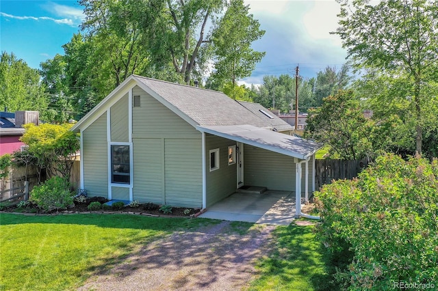 exterior space featuring fence, driveway, a shingled roof, a carport, and a lawn