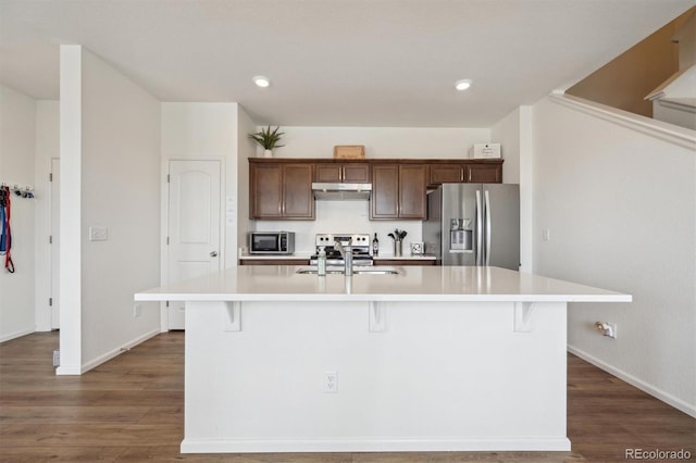 608 N Bersshine Ct, Aurora, CO 80137 - kitchen with appliances with stainless steel finishes, under cabinet range hood, light countertops, a kitchen breakfast bar, and dark wood-style floors