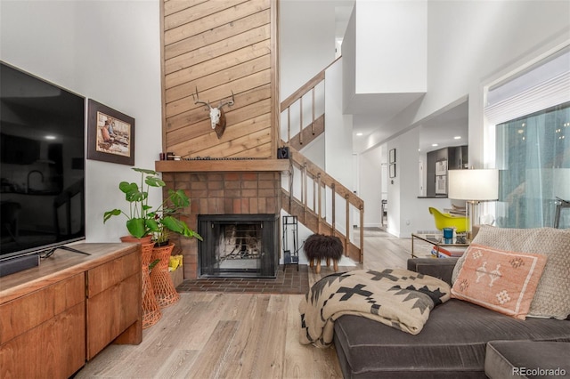 living room featuring a fireplace, a towering ceiling, light wood finished floors, and stairs