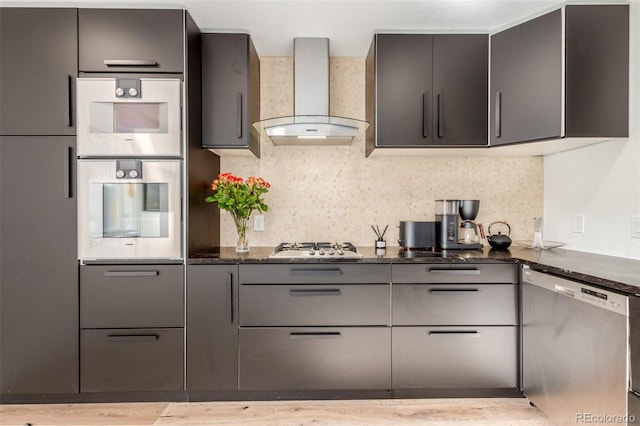 kitchen featuring backsplash, appliances with stainless steel finishes, wall chimney range hood, modern cabinets, and dark stone counters