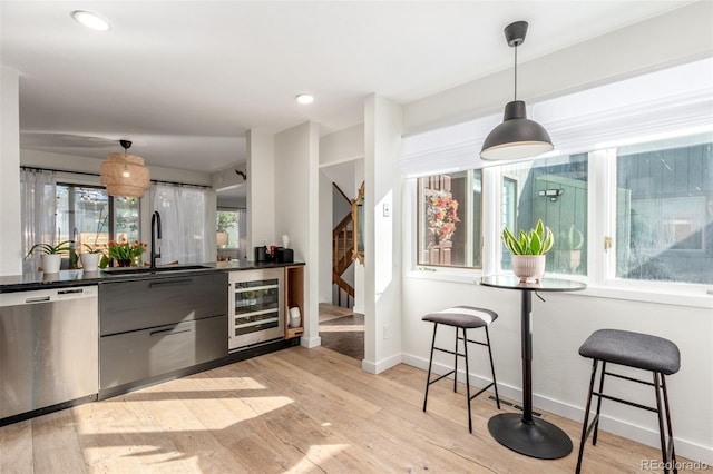 kitchen featuring dark countertops, wine cooler, decorative light fixtures, stainless steel dishwasher, and a sink