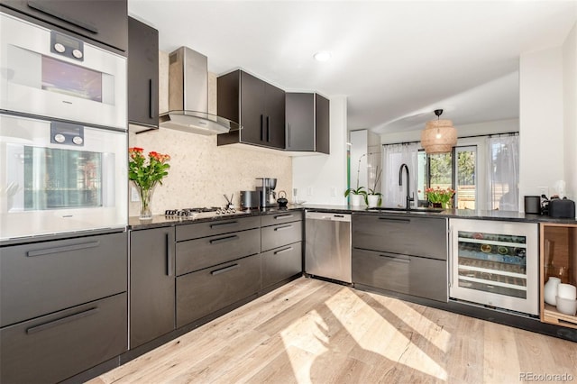 kitchen with beverage cooler, wall chimney exhaust hood, modern cabinets, appliances with stainless steel finishes, and a sink