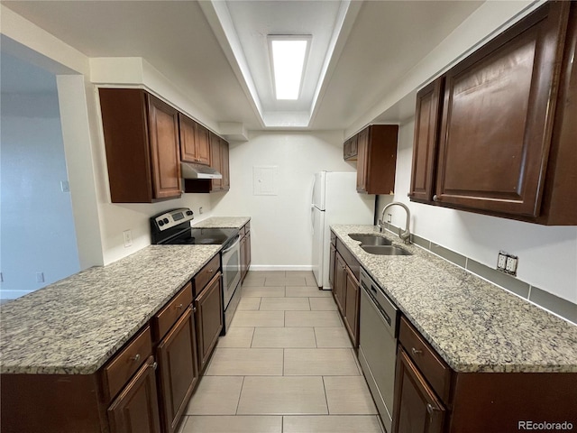 kitchen featuring light stone counters, under cabinet range hood, stainless steel appliances, a sink, and baseboards