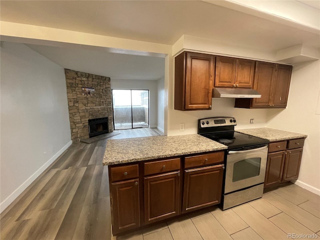 kitchen featuring under cabinet range hood, electric range, a fireplace, and light wood finished floors