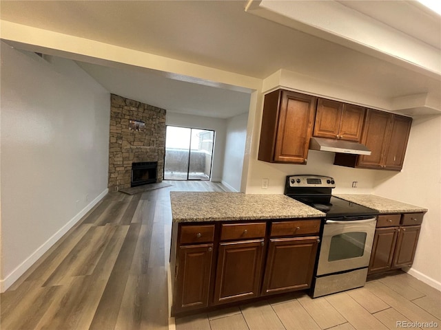 kitchen with light wood-style floors, a stone fireplace, stainless steel electric range oven, and under cabinet range hood