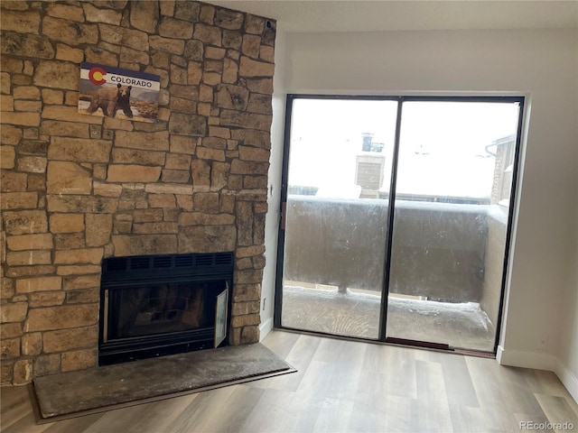 interior space with a stone fireplace, baseboards, and wood finished floors