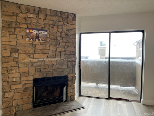 unfurnished living room with a textured ceiling, a stone fireplace, and wood finished floors