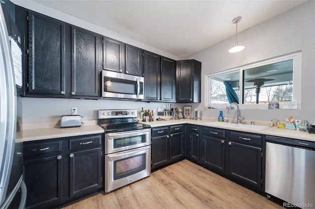 kitchen featuring sink, light wood-type flooring, hanging light fixtures, and stainless steel appliances