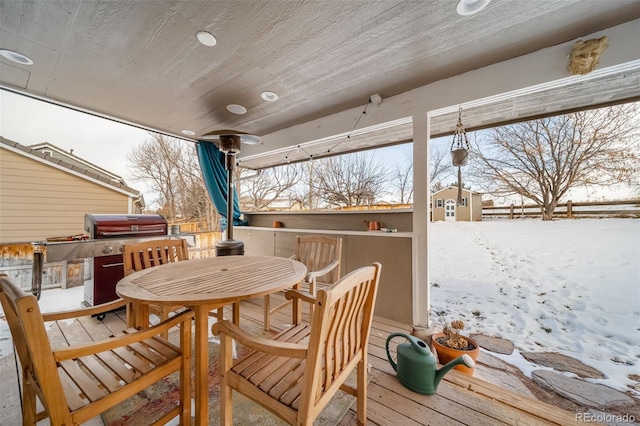 snow covered deck featuring a hot tub, a storage shed, and grilling area