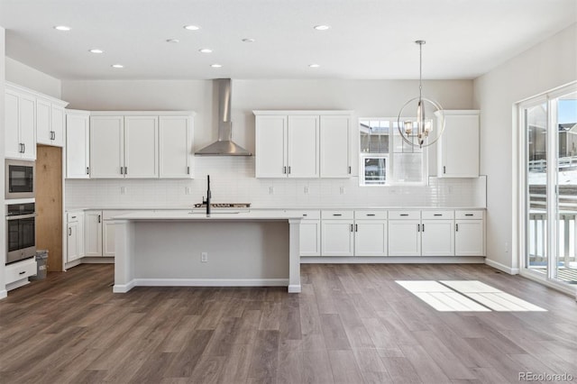 kitchen with dark hardwood / wood-style flooring, wall chimney range hood, oven, and white cabinets