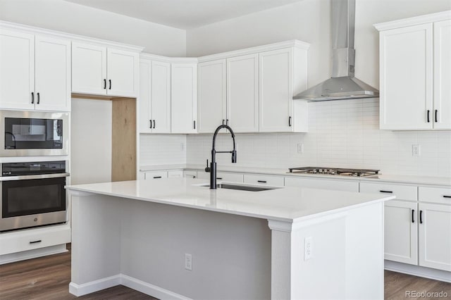 kitchen with wall chimney range hood, sink, a kitchen island with sink, white cabinetry, and stainless steel appliances