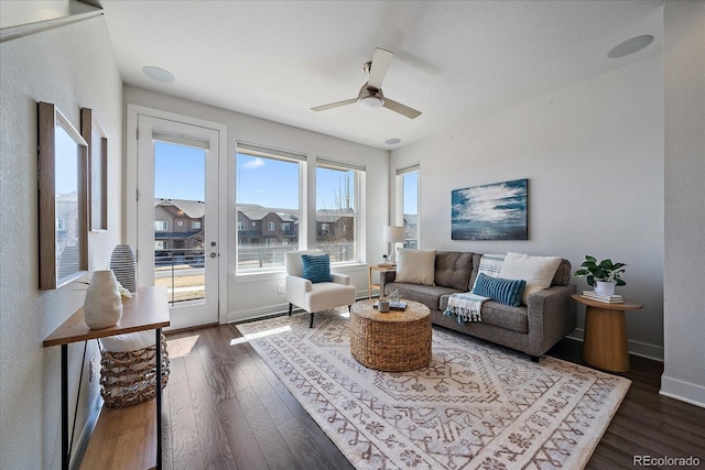 living room featuring dark wood-type flooring, a ceiling fan, and baseboards