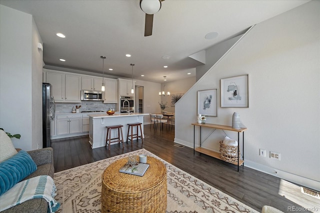 living area featuring recessed lighting, ceiling fan with notable chandelier, dark wood-type flooring, and baseboards