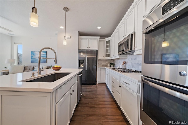 kitchen with a sink, backsplash, dark wood finished floors, appliances with stainless steel finishes, and light countertops