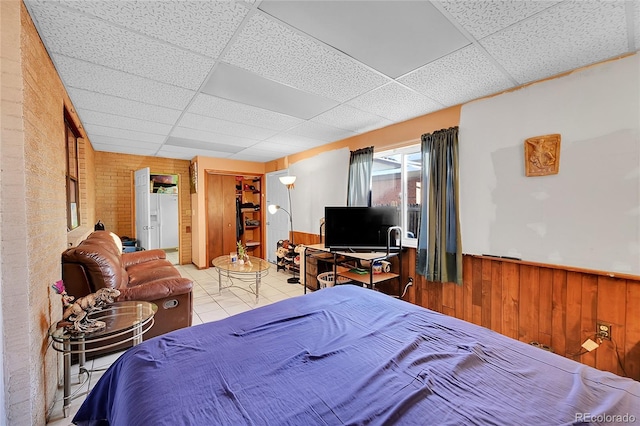 tiled bedroom featuring a paneled ceiling and wood walls