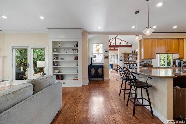 kitchen featuring stone countertops, pendant lighting, built in features, a kitchen bar, and dark wood-type flooring