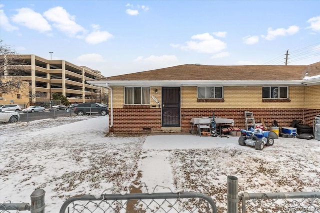 snow covered house featuring brick siding and fence